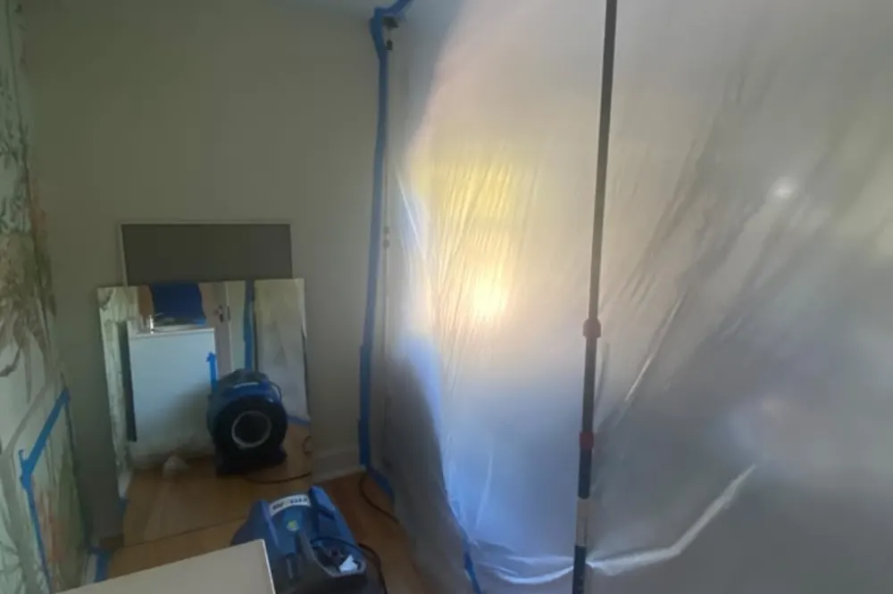 HEPA air scrubber running inside plastic containment in a bedroom