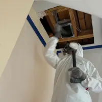 Mold technician in protective suit and respirator opening a ceiling